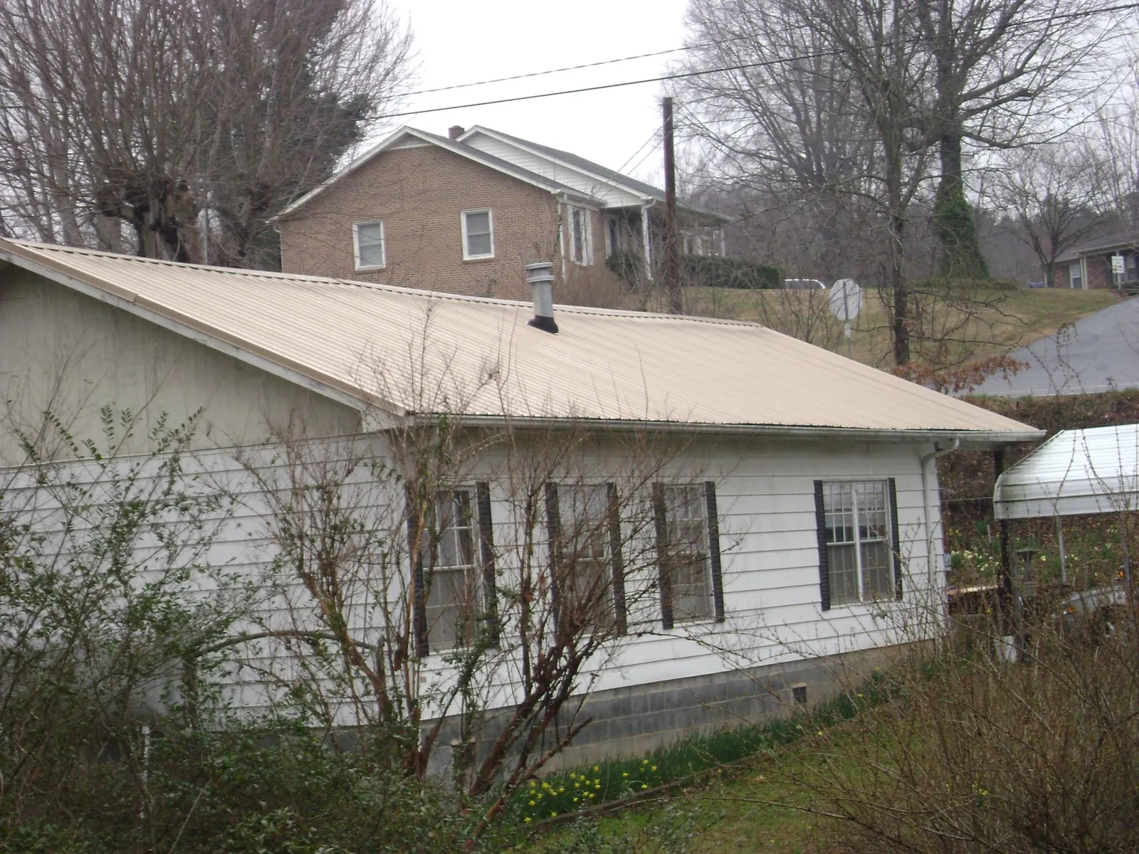 Tan metal roof on a white sided house set into a hillside — Commercial Roofing by Roofing Brothers in Port Ludlow
